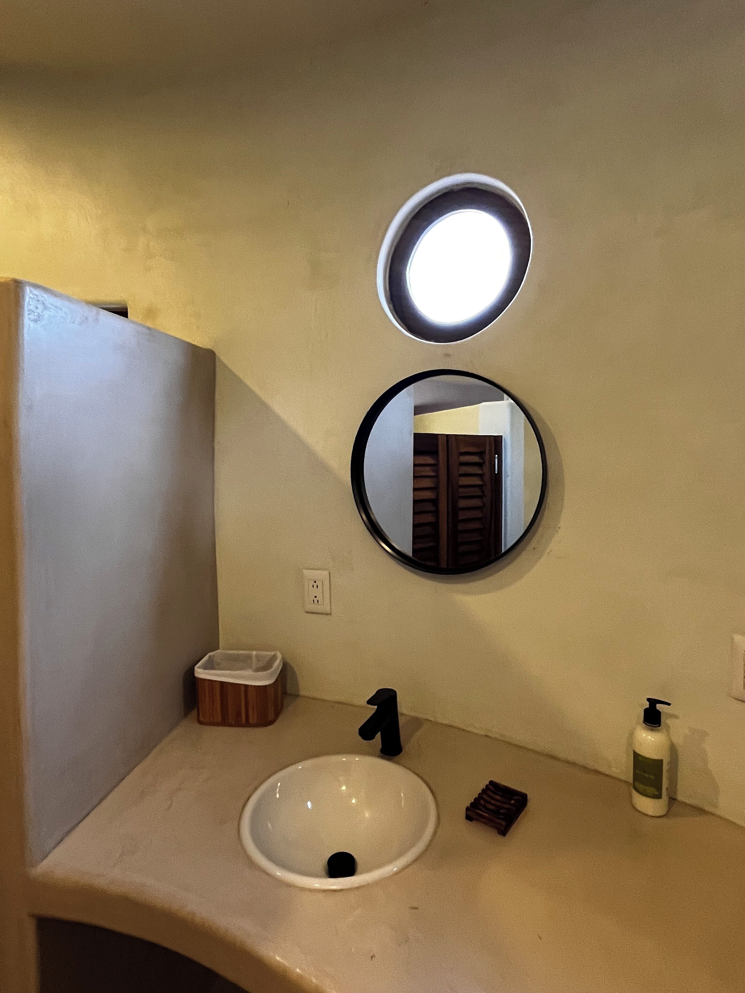 Un baño con un lavabo blanco, un espejo redondo y una lámpara sobre el espejo.