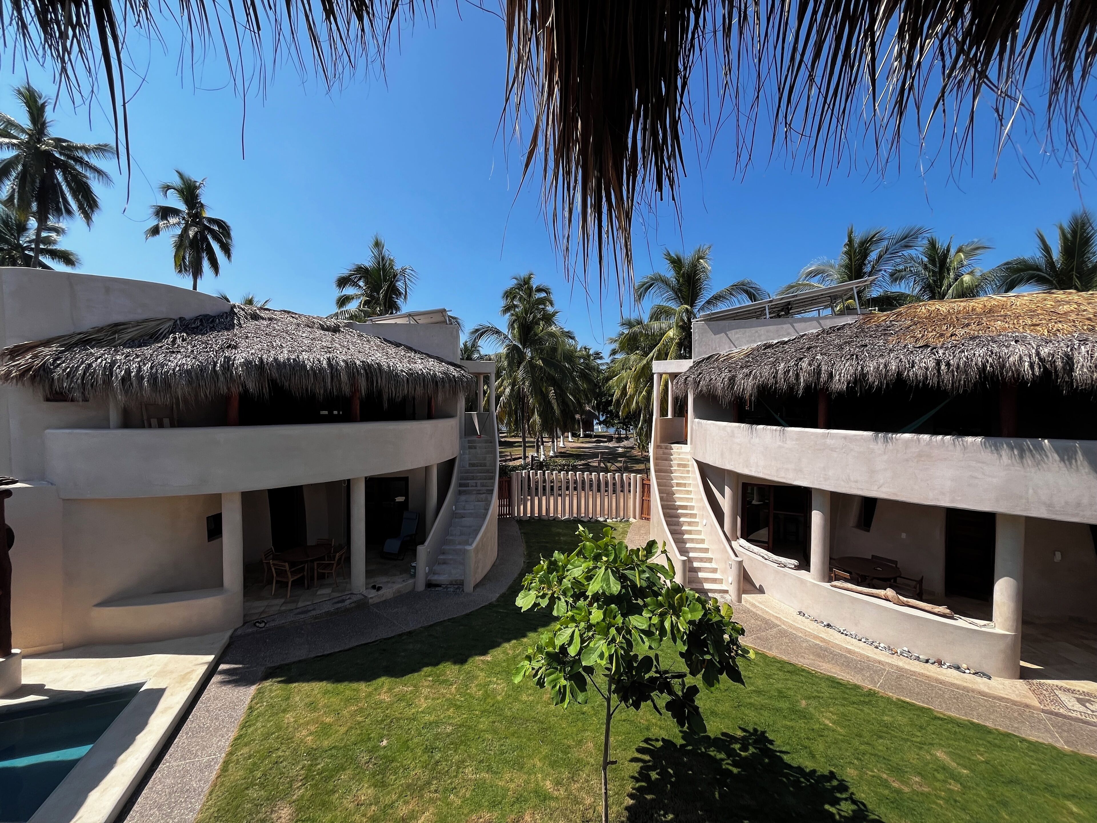 Un resort con edificios de techo de paja, piscina y palmeras.