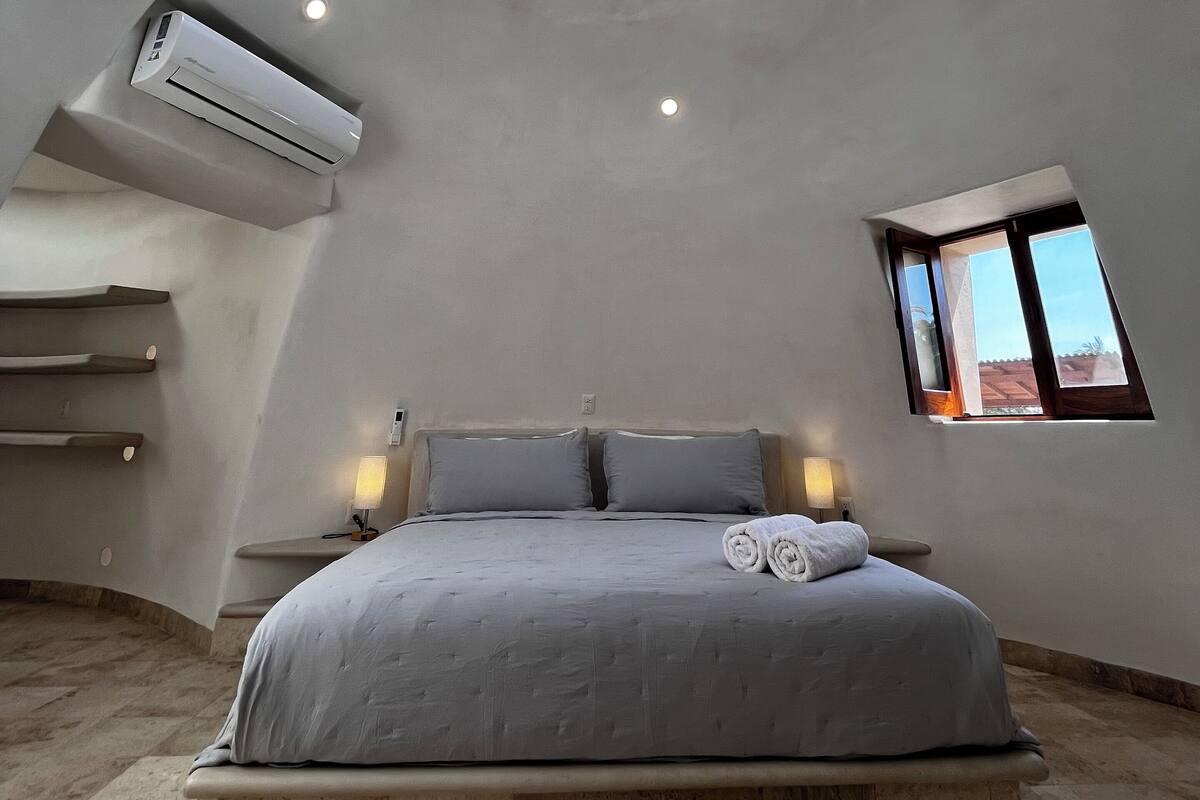A spacious bedroom with a skylight, a bed with a headboard, and a small window.