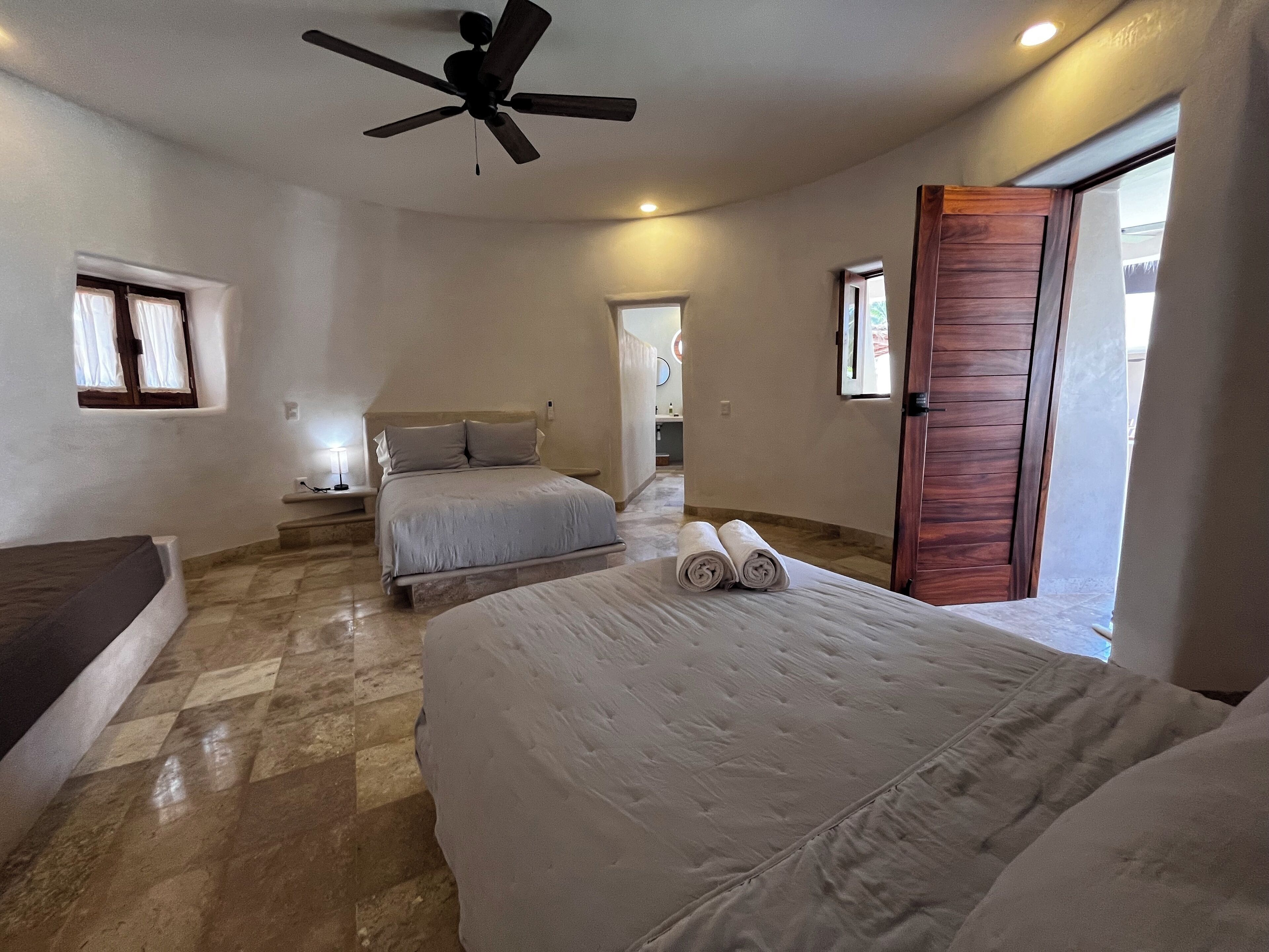 A bedroom with two beds, a ceiling fan, and a wooden door.