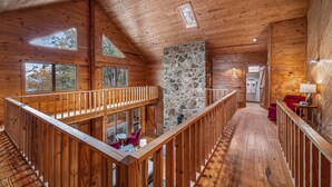 A wooden cabin interior with a stone fireplace, wooden railings, and a balcony with outdoor seating. - Snail’s Pace South-6br/3.5 bath w/gorgeous views (Fort Payne)