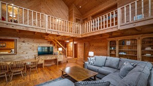 A spacious wooden cabin with a loft bedroom, a dining area, and a living room with a sofa and TV. - Snail’s Pace South-6br/3.5 bath w/gorgeous views (Fort Payne)