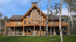 A large log cabin with a stone chimney, wooden balconies, and a stone foundation. - Remote Cabin near Warm River (Ashton)
