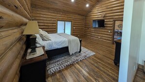 A log cabin bedroom with a bed, bedside lamp, and a small table. - Remote Cabin near Warm River (Ashton)