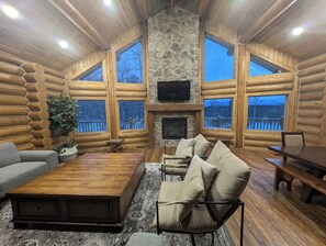 A log cabin interior with a stone fireplace, large windows, and a cozy seating area. - Remote Cabin near Warm River (Ashton)