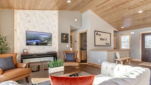 Uma sala de estar espaçosa com lareira, televisão fixada em uma parede texturizada e um espaço de estar aconchegante com sofá e poltronas.