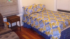 Een slaapkamer met een bed, een stoel, een nachtkastje en een raam met jaloezieën.