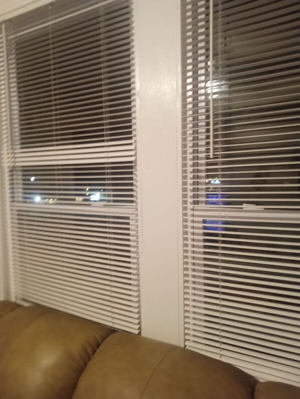 Ein Zimmer mit zwei Fenstern, horizontalen Jalousien, einem braunen Ledersofa und einer weißen Wand.