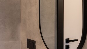 Ein modernes Badezimmer mit einem großen, ovalen Spiegel, einer schwarzen Türgriff und einem Lichtschalter an der Wand.