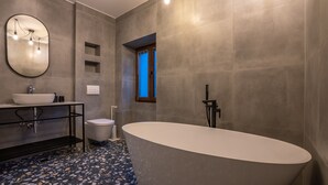 Ein modernes Badezimmer mit freistehender Badewanne, einem runden Spiegel, einem Waschbecken mit Aufsatzbecken und einer Toilette.