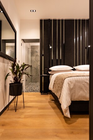 A modern bedroom with a large bed, a potted plant, a bedside table, and a mirror. - City Premium Heritage Hotel (Zadar)