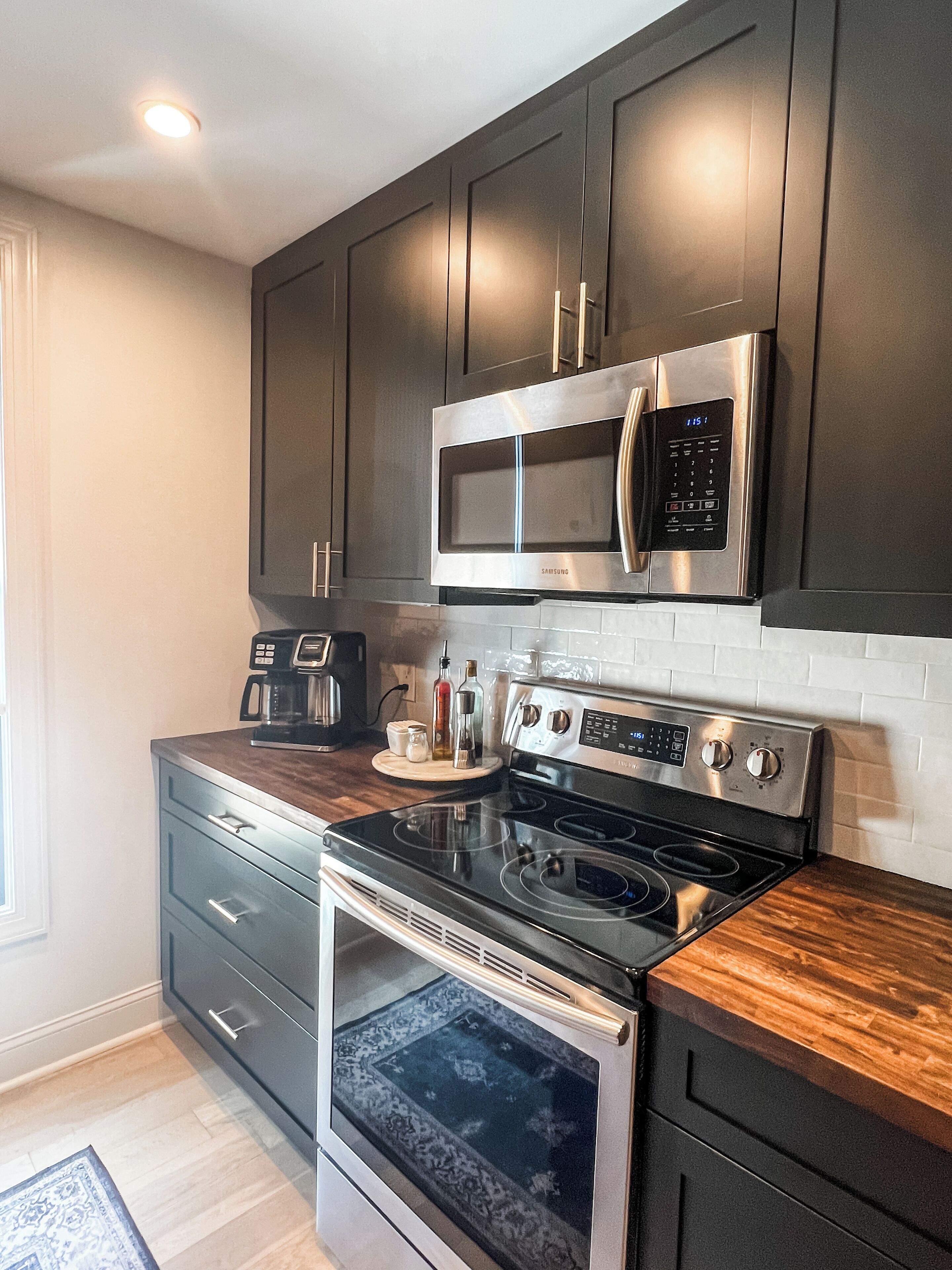 A modern kitchen with dark cabinetry, stainless steel appliances, and a wood countertop.