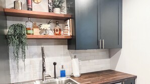 Cocina moderna con armarios oscuros, un lavaplatos de acero inoxidable y un lavavajillas. Hay repisas de madera sobre el fregadero con varios objetos y una planta colgante.