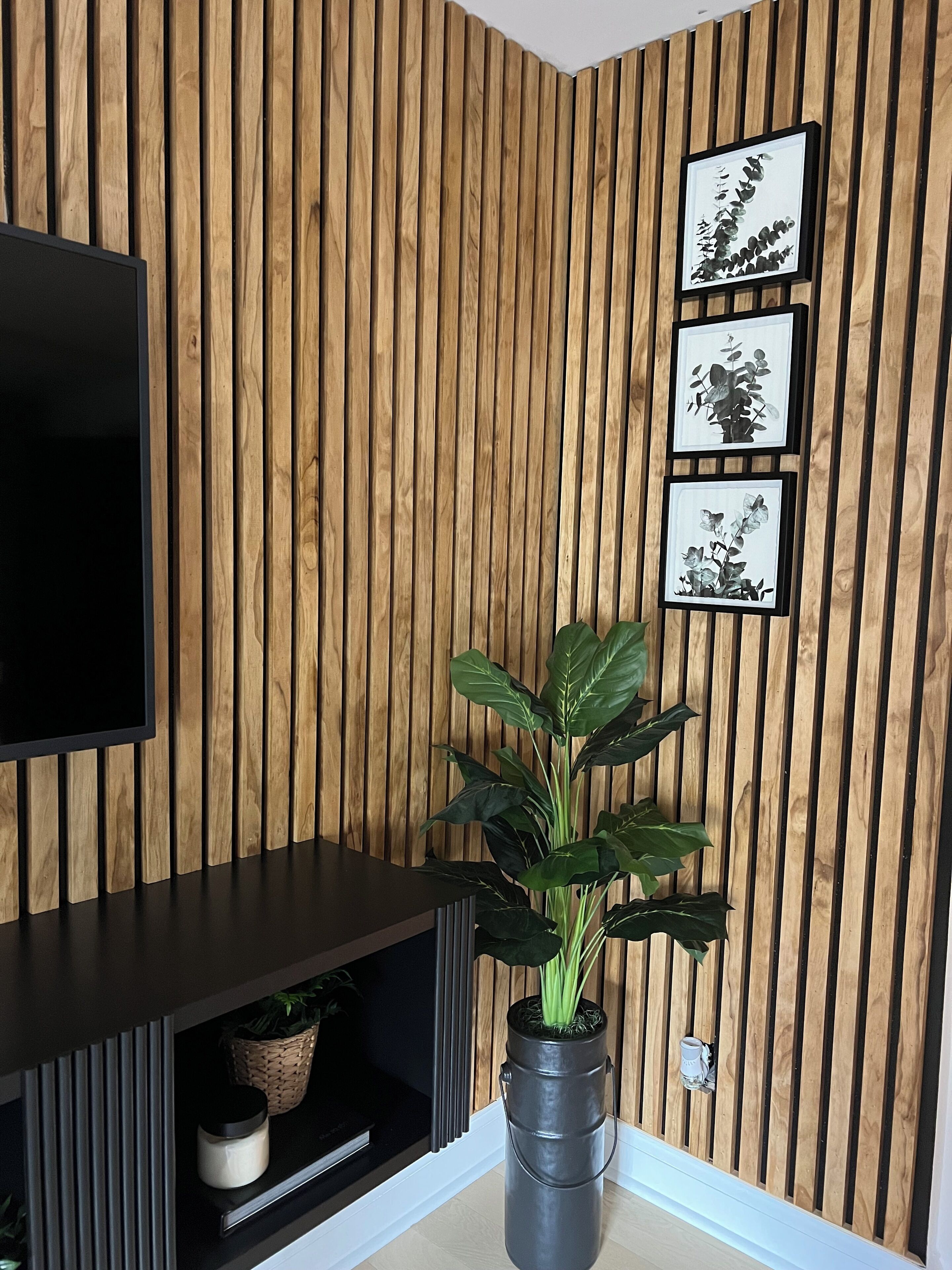 Een moderne woonkamer met een wand van houten latten, een flatscreen televisie, een donkere entertainmentkast en een potplant.