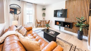 Una sala de estar moderna con un sofá de cuero, una mesa de comedor con sillas, un televisor montado en la pared y una pared decorativa de madera.