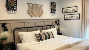 Un dormitorio ordenado con cama, mesitas de noche, decoración en la pared y una alfombra estampada.