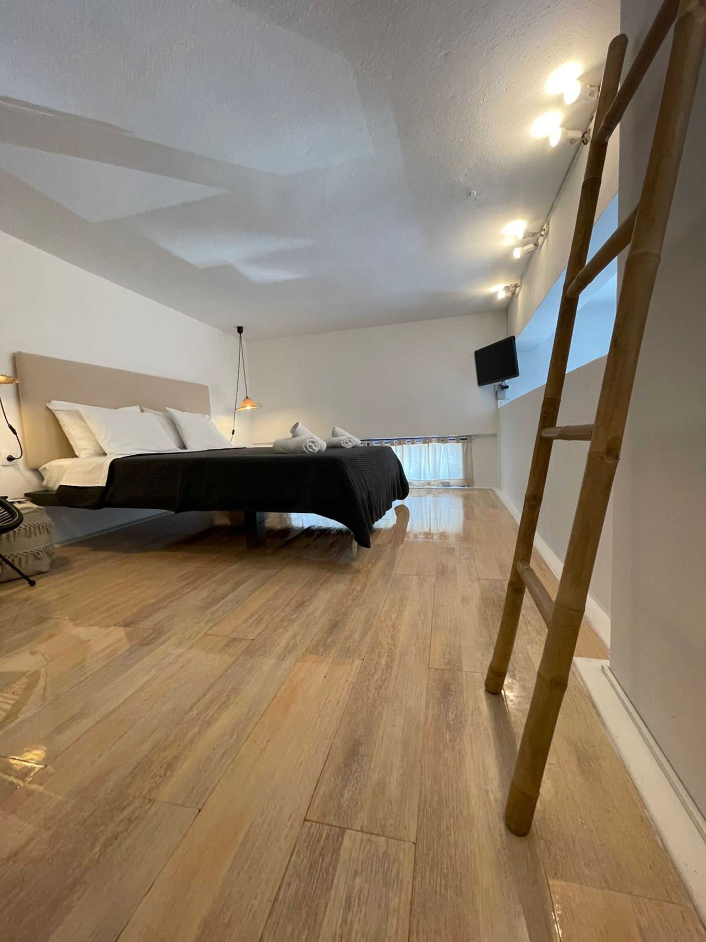 Una camera da letto con un letto, pavimento in legno, una scala, una televisione e una finestra con tende.