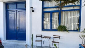 A blue door, a window with curtains, and outdoor seating with potted plants. - Stella's Loft In Center Of Tinos (Tinos)