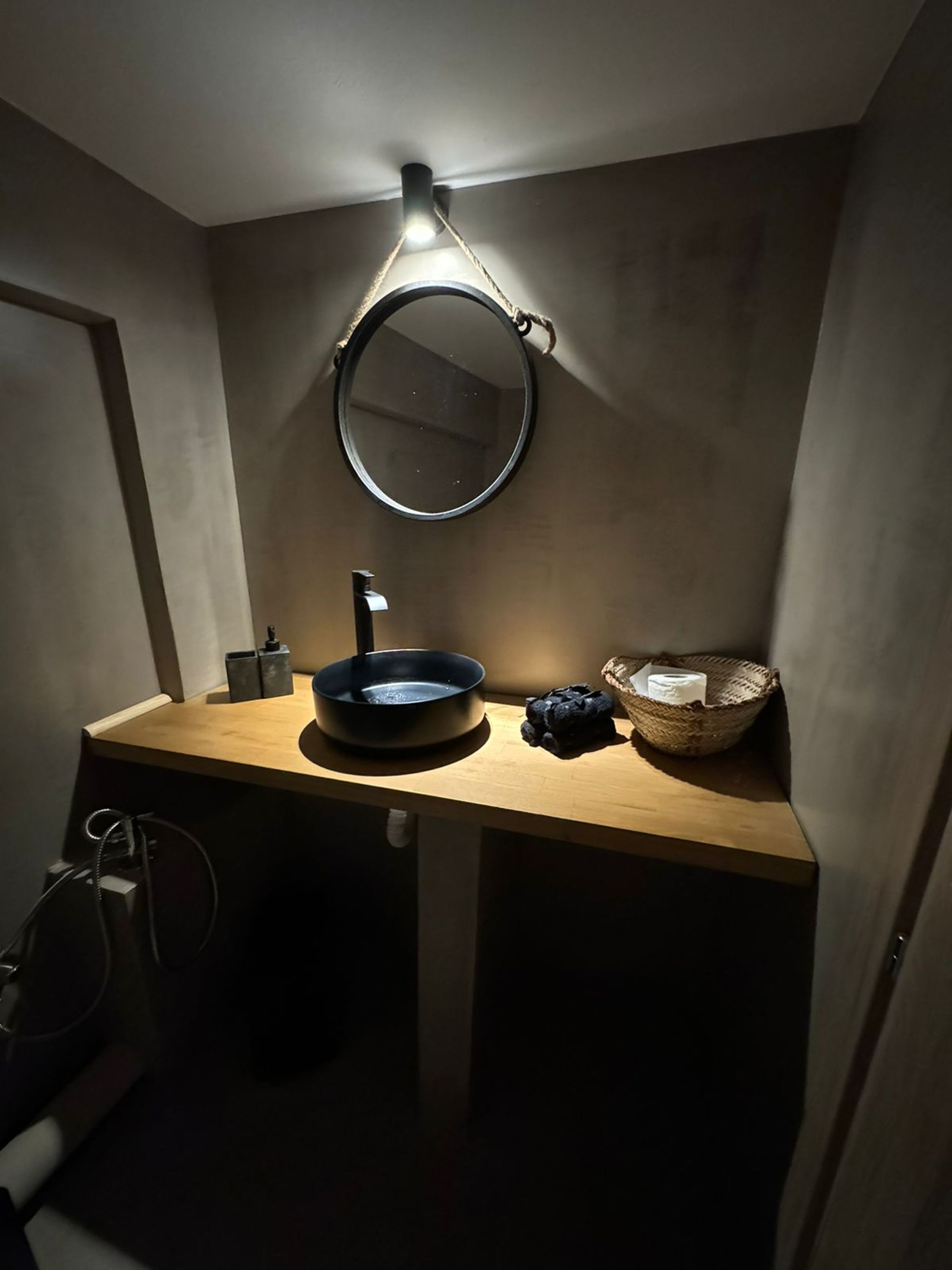 Un baño pequeño con un espejo redondo, un lavamanos y una cesta.