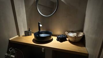 Un baño pequeño con un espejo redondo, un lavamanos y una cesta.