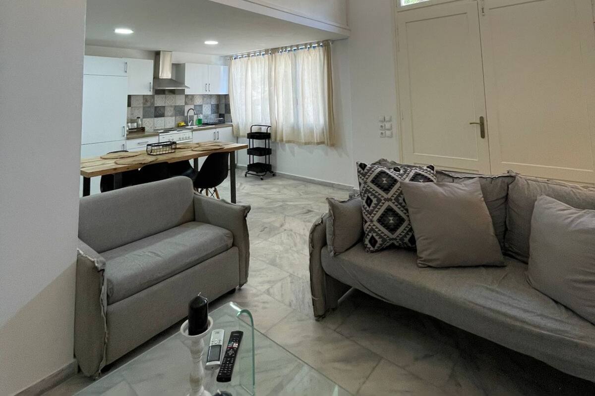 A modern living room with a glass coffee table, two sofas, and a kitchen in the background.