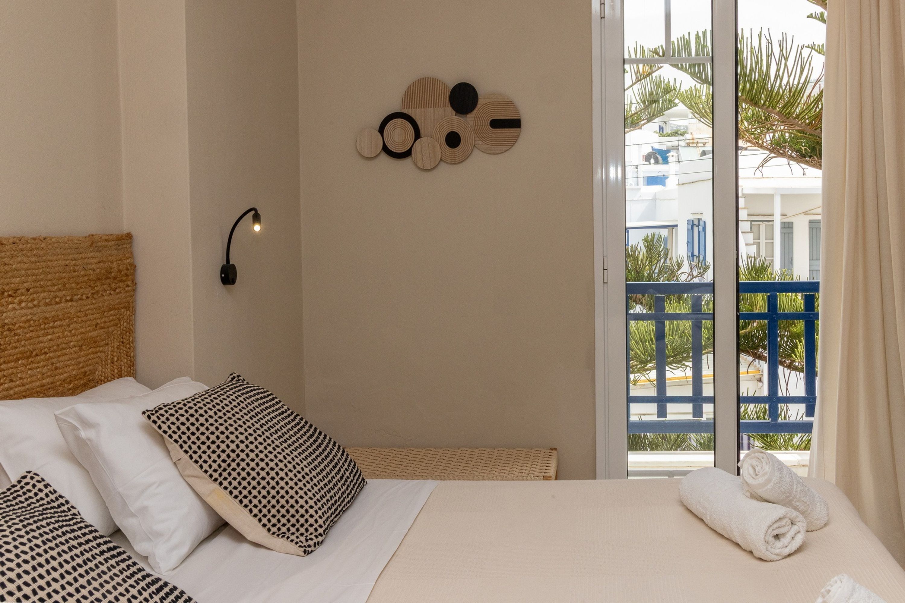 A bedroom with a bed, pillows, a wall art piece, and a view of a blue balcony.