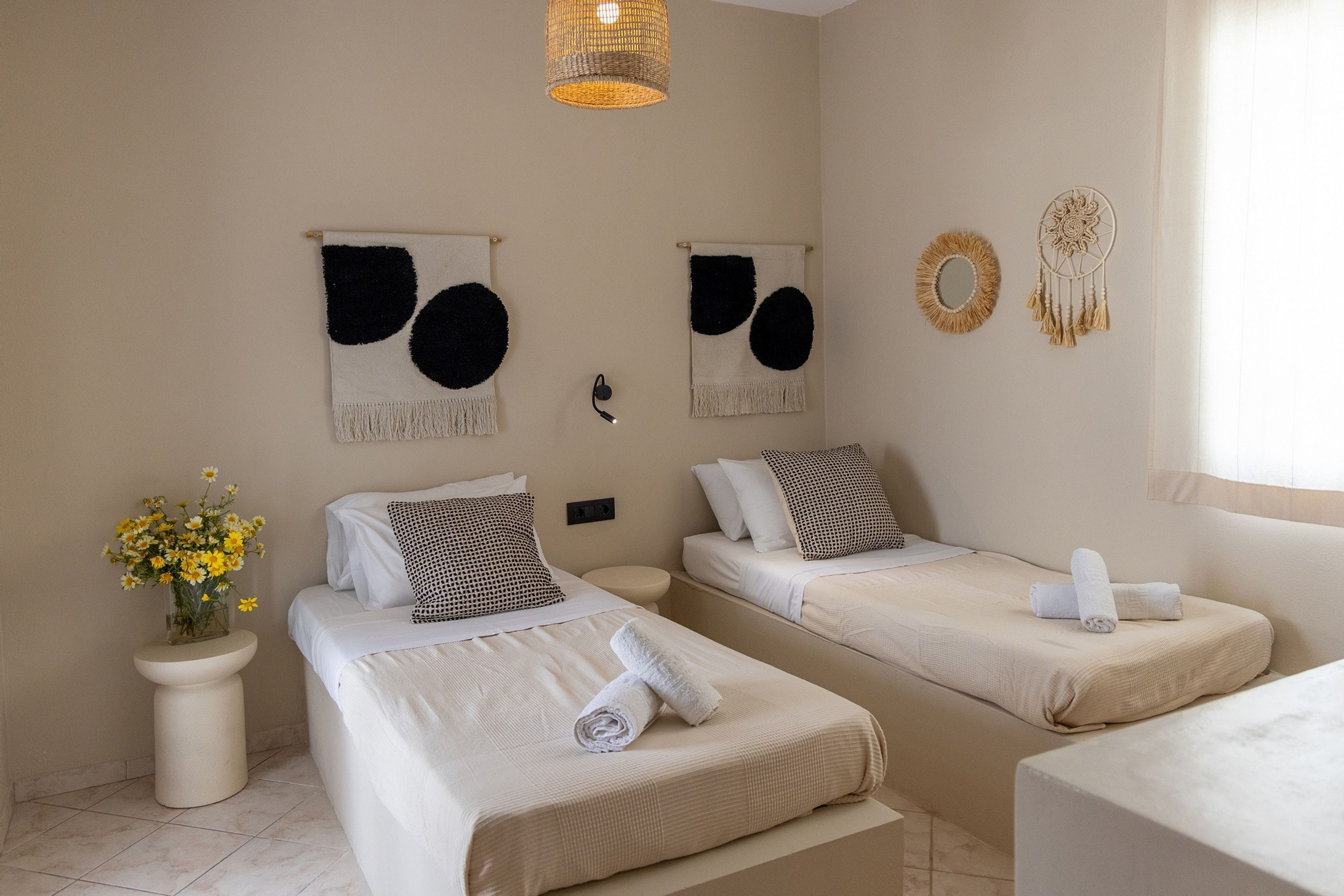 A hotel room with two beds, a bedside table with a vase of flowers, and wall decorations including dream catchers.