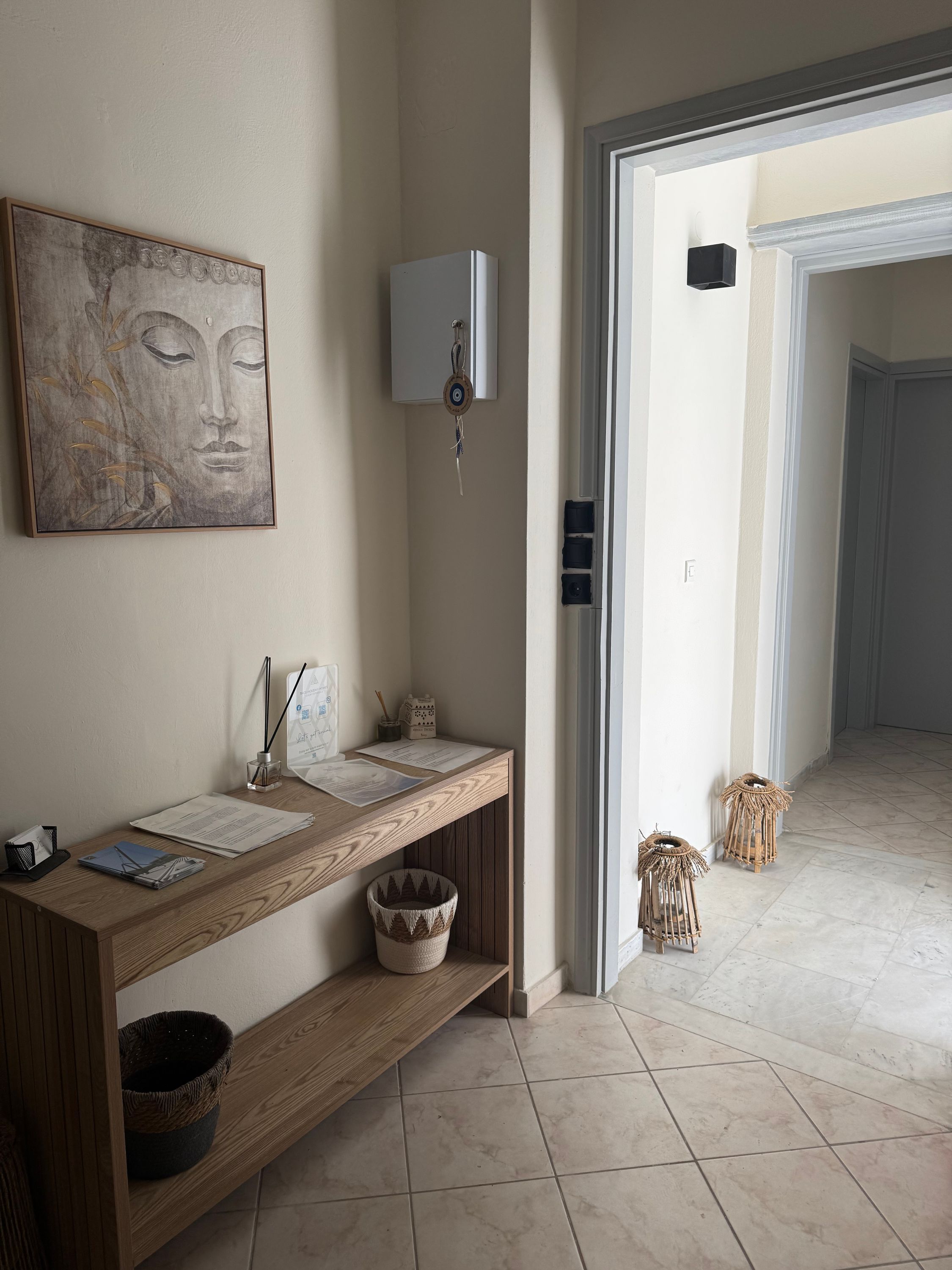A hallway with a wooden console table, a wall-mounted light, a framed artwork, and a door leading to another room.