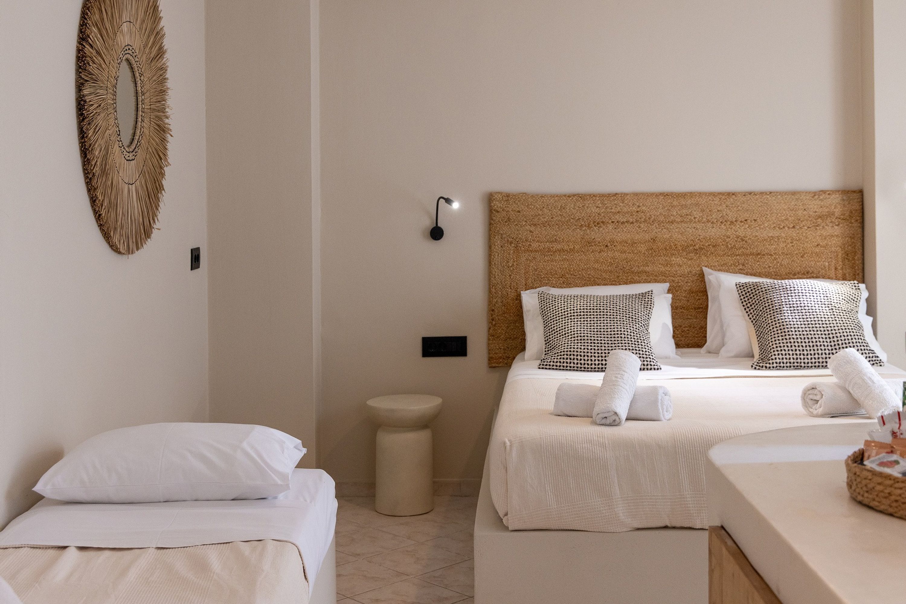 Ein Hotelzimmer mit zwei Betten, einem gewobenen Kopfteil, einem kleinen runden Tisch und einer Wandleuchte.