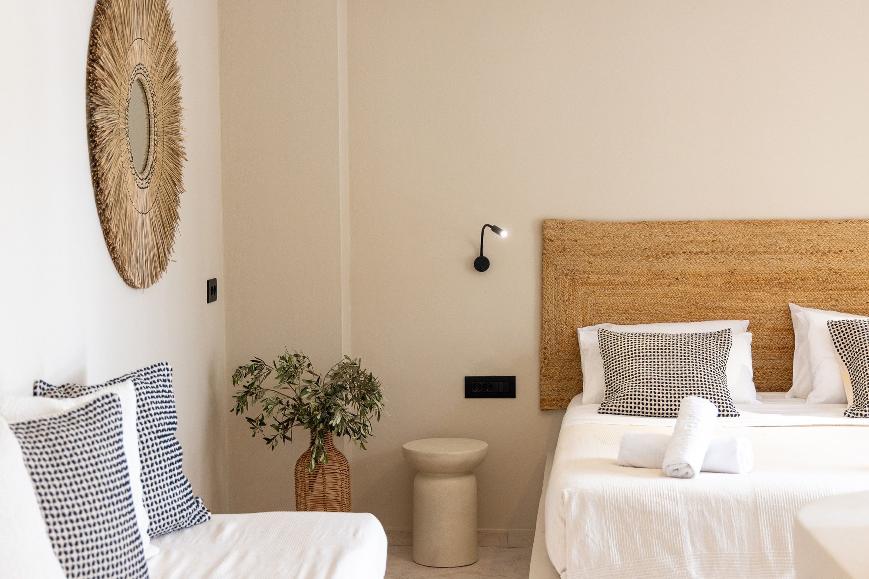 A hotel room with two beds, a large mirror, a wall-mounted light, and a small round table with a plant.