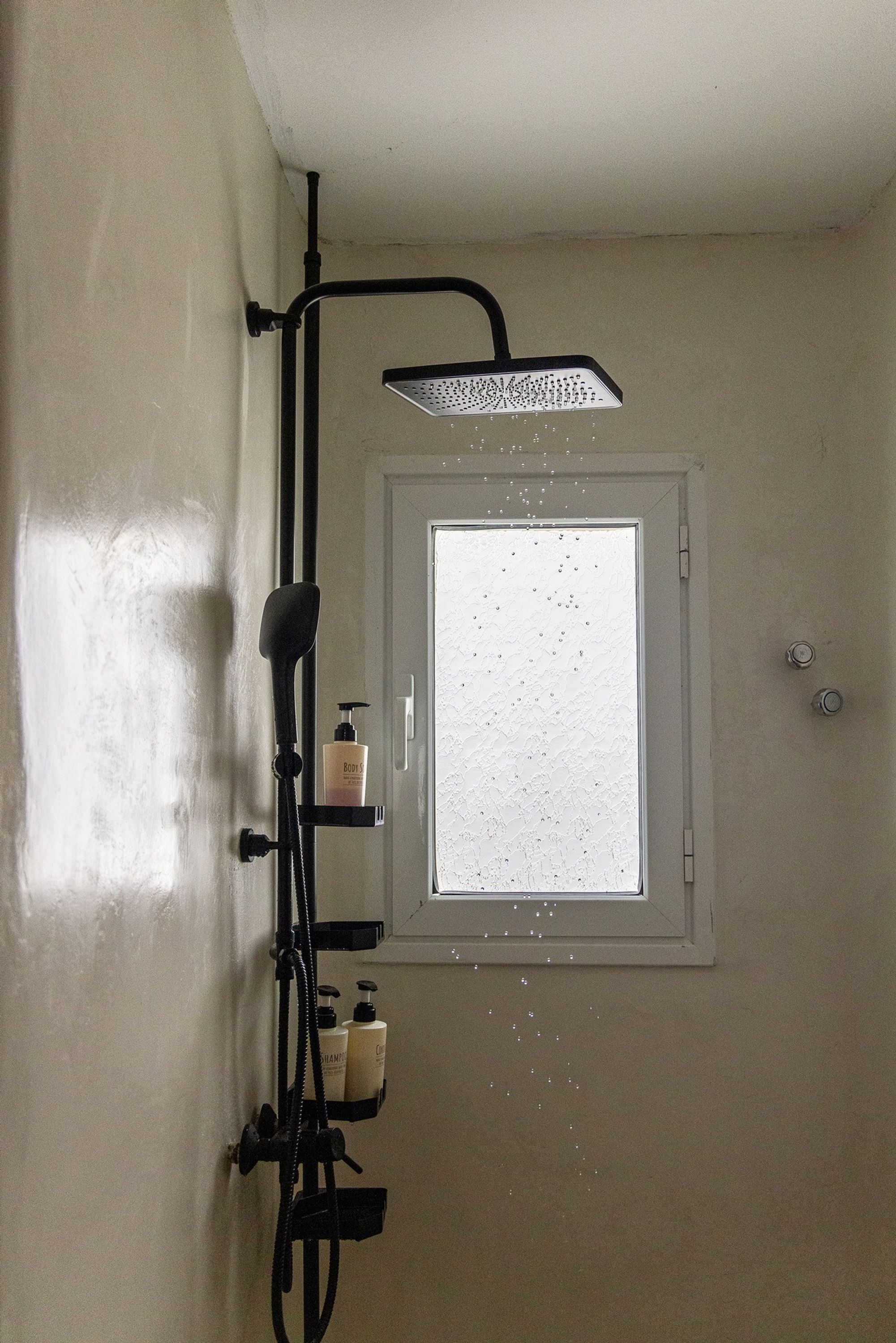 Ducha con cabezal de ducha de mano y una ventana encima.