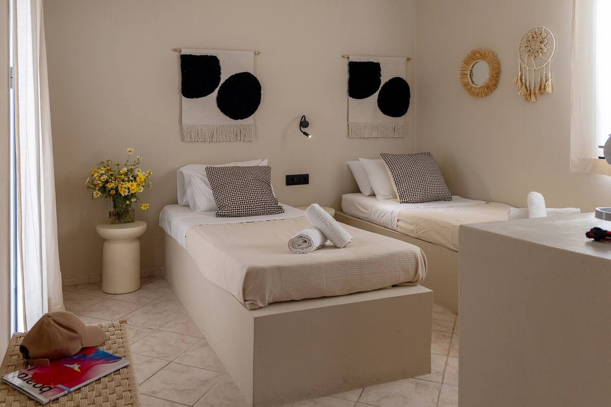 A hotel room with two beds, a small bedside table with a vase of flowers, and wall decor including dreamcatchers.