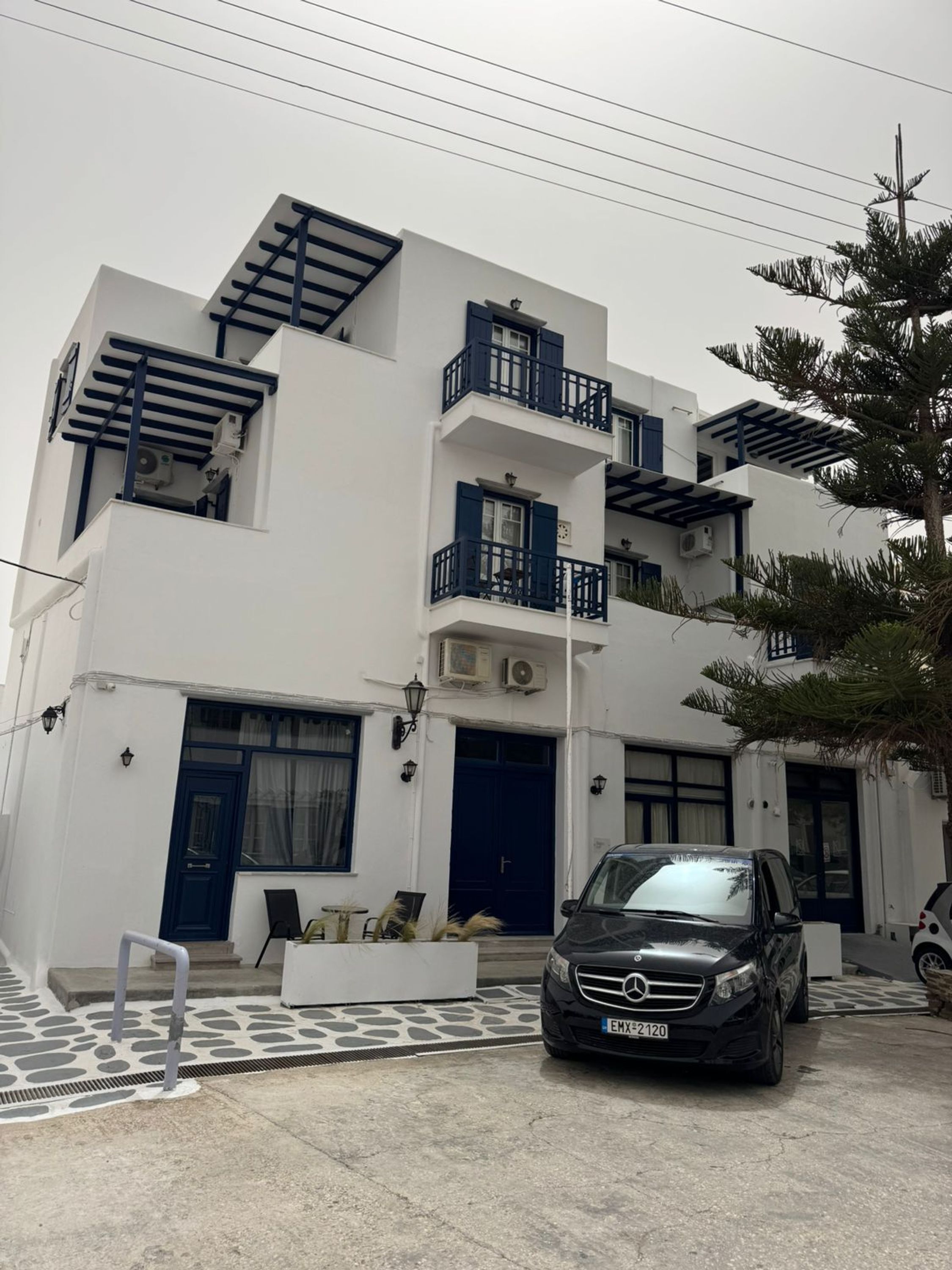 A modern multi-story building with balconies, a car parked in front, and a palm tree nearby.