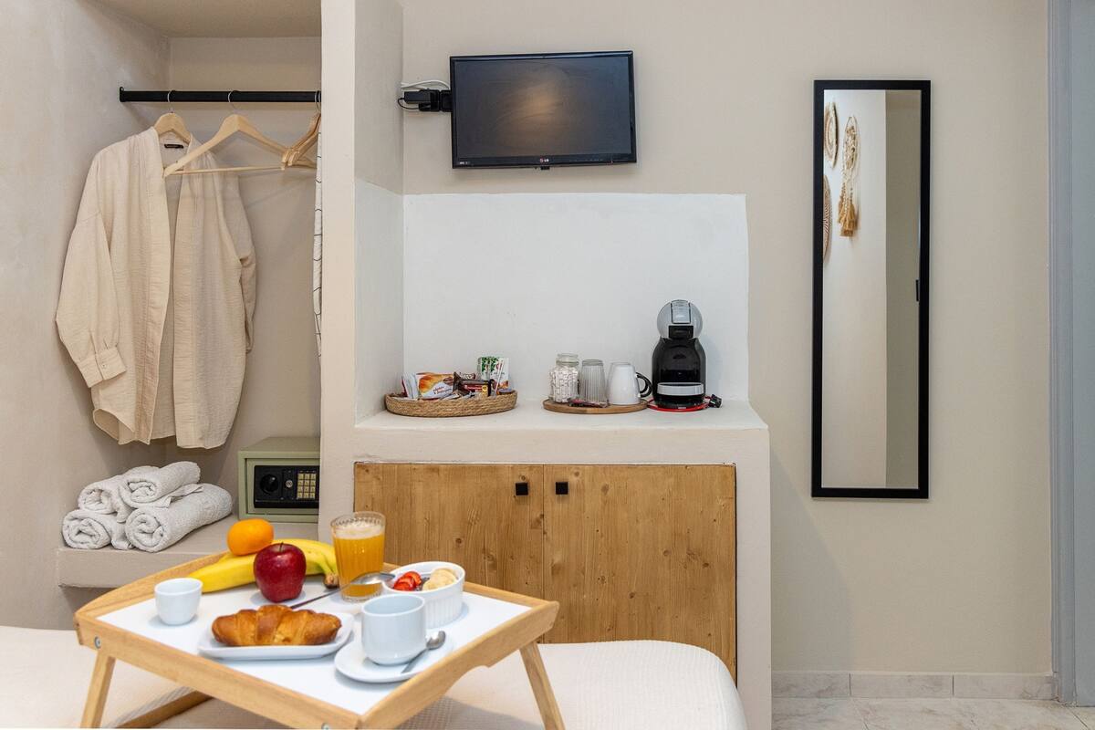 A hotel room with a bed, a bedside table with breakfast items, a TV mounted on the wall, and a mirror.