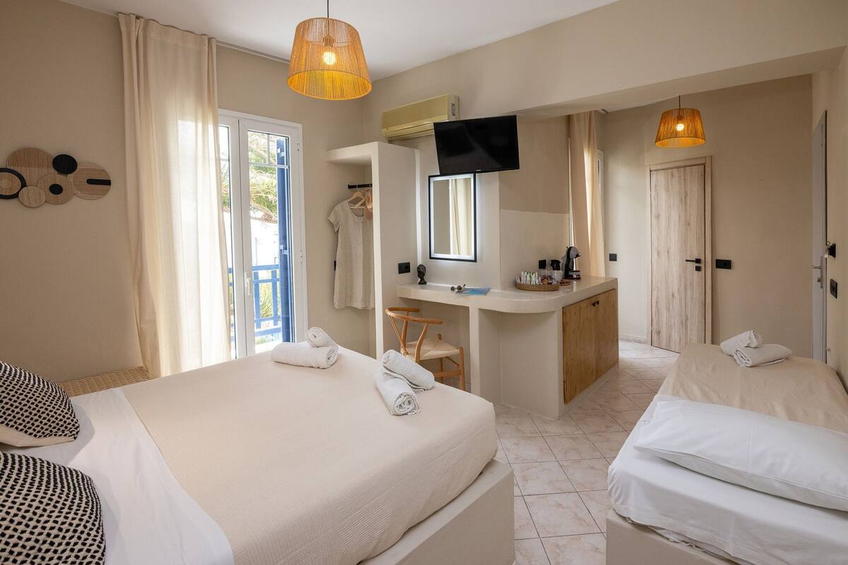 A hotel room with two beds, a desk, a TV, and a bathroom.