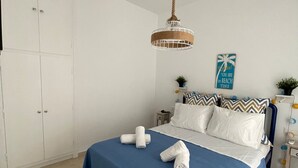 A neatly made bed with a blue bedspread and white pillows, a hanging rattan light fixture, and a wall poster. - Zen Beach House in Tinos 2 (Tinos)
