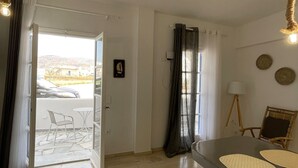 A modern kitchen with a large island, a dining area with a table and chairs, and a view of the outside through a glass door. - Zen Beach House in Tinos 2 (Tinos)