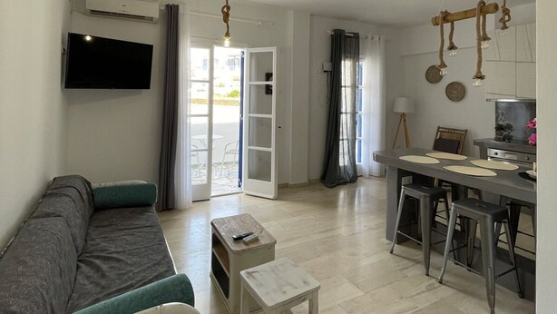 A modern living room with a sofa, a small table, a TV, and a kitchen area with stools. - Zen Beach House in Tinos 2 (Tinos)