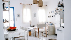 Une cuisine lumineuse et bien éclairée, avec des meubles blancs, une table à manger entourée de chaises et un réfrigérateur décoré d’aimants et de photos.