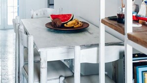 Un coin repas avec une table et des chaises blanches, une assiette remplie de nourriture et un luminaire suspendu.