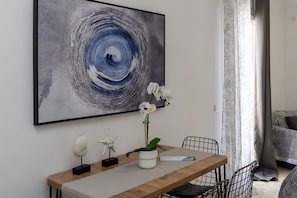 A dining area with a wooden table, chairs, a white orchid in a white pot, a starfish decoration, and a large abstract painting on the wall. - Zen Beach House in Tinos 1 (Tinos)