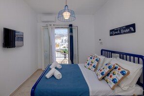 A neatly made bed with blue bedding and decorative pillows, a television mounted on the wall, and a sign welcoming guests to the beach house. - Zen Beach House in Tinos 1 (Tinos)