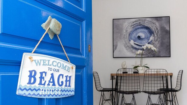 A blue door with a 'Welcome to our Beach House' sign and a dining area with a table and chairs. - Zen Beach House in Tinos 1 (Tinos)
