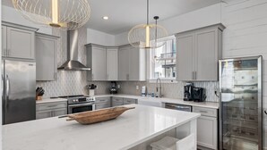 A modern kitchen with white cabinetry, a large island, stainless steel appliances, and pendant lighting. - Beach🏖️Service! Rooftop Deck-Private Pool-LSV (Golf Cart)-Bikes🚲-8BR Palm Paradi (Miramar Beach)