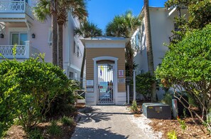 A pathway leading to a building with a gated entrance, surrounded by lush greenery and palm trees. - Beach🏖️Service! Rooftop Deck-Private Pool-LSV (Golf Cart)-Bikes🚲-8BR Palm Paradi (Miramar Beach)
