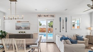 A spacious living area with a dining table, chairs, a sofa, and a view of a swimming pool through glass doors. - Beach🏖️Service! Rooftop Deck-Private Pool-LSV (Golf Cart)-Bikes🚲-8BR Palm Paradi (Miramar Beach)
