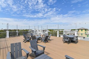 A deck with outdoor seating, string lights, and a view of buildings in the background. - Beach🏖️Service! Rooftop Deck-Private Pool-LSV (Golf Cart)-Bikes🚲-8BR Palm Paradi (Miramar Beach)