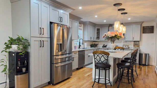 A modern kitchen with stainless steel appliances, grey cabinetry, and a central island with bar stools.