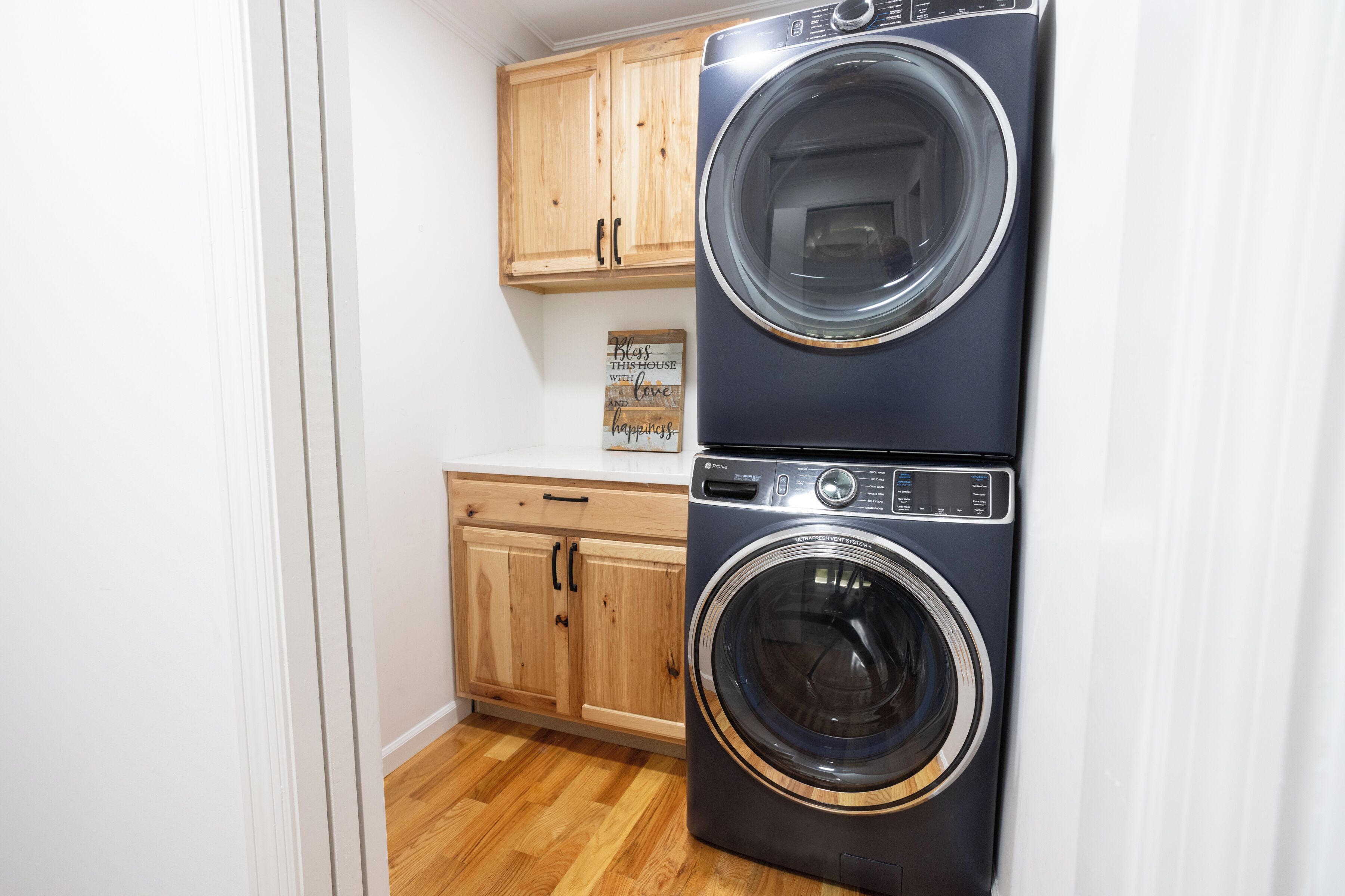 A laundry room with a stacked washer and dryer, wooden cabinets, and a wooden floor.