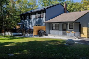 A two-story house with a covered patio, a wooden deck, and a large rock in the yard. - Spacious 5-bedroom house in the woods in Cold Spring just 5 minutes from town (Cold Spring)